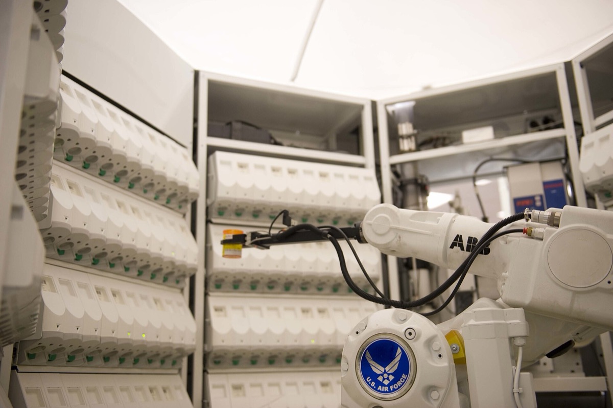 Robotic arm in an automated pharmacy dispensing system before a wall of medication cassettes.
